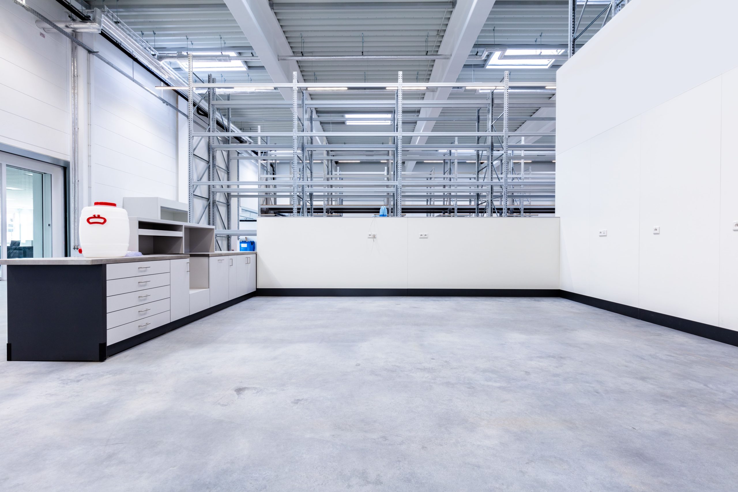 Empty industrial storage room with metal shelving, cabinets, and a large white container on a countertop.