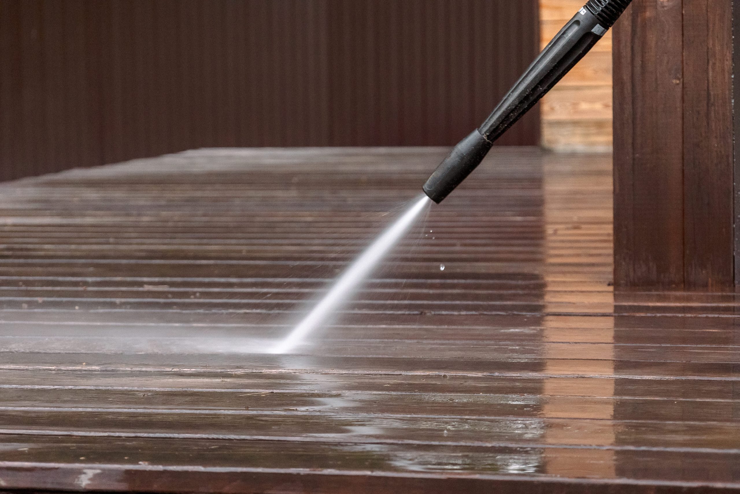 Pressure washer cleaning a wooden deck, showing a clear difference between cleaned and uncleaned areas.